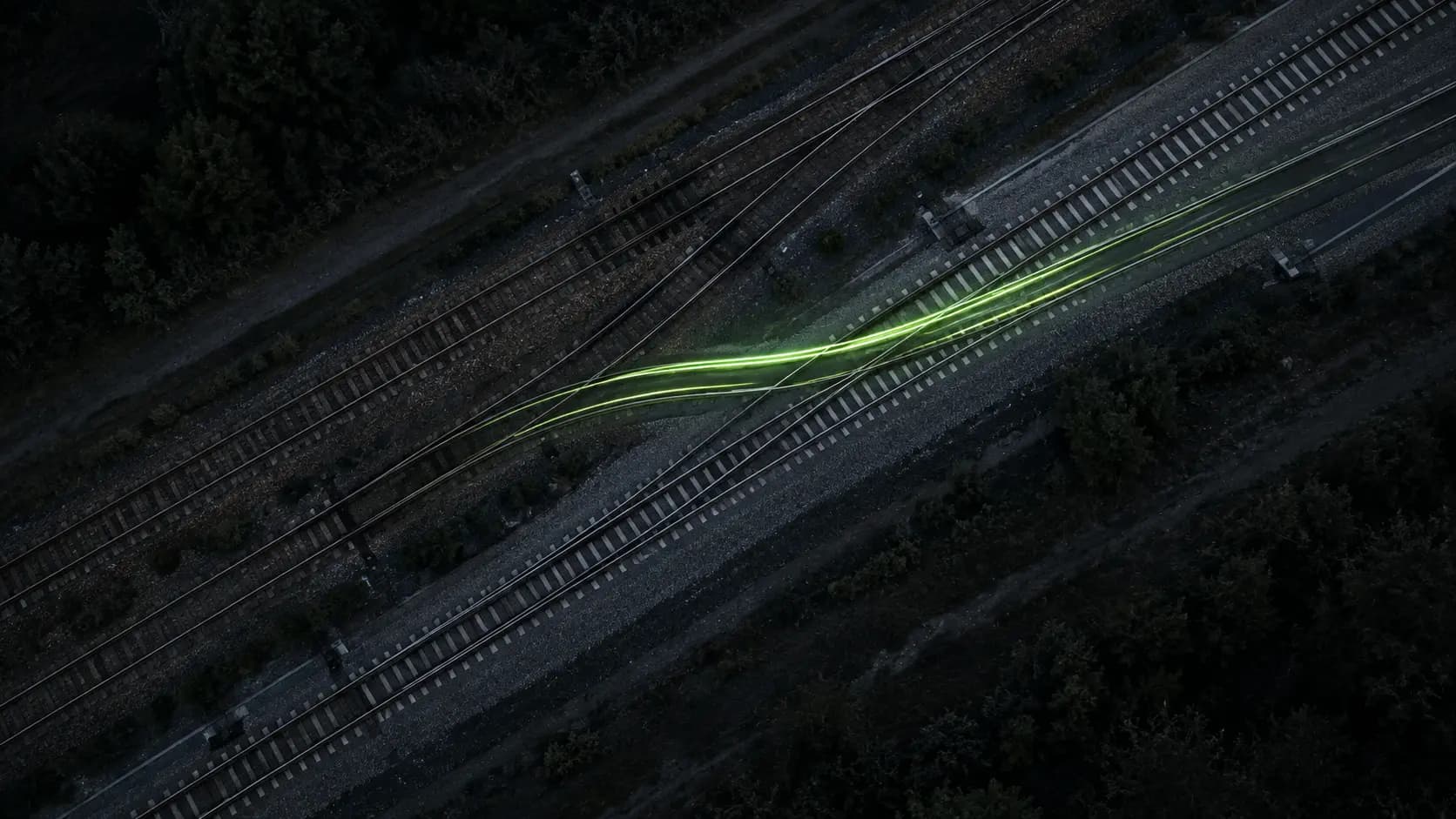 Aerial view of parallel railway tracks with a green light trail crossing from one to the other